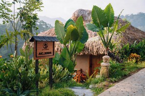 A thatched-roof hut with a wooden sign in front, surrounded by lush greenery and a clear view of distant mountains. - An Chang Retreat & Spa (Ha Giang 1)