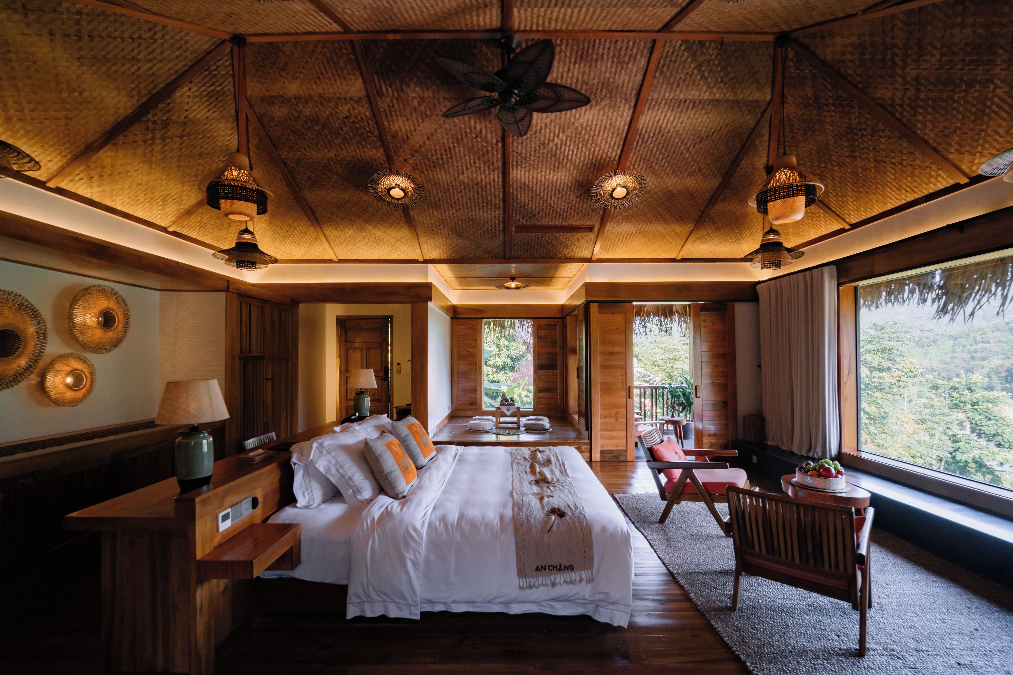 Un dormitorio amplio con una cama grande, un escritorio y una silla. Se ve el exterior a través de la ventana.