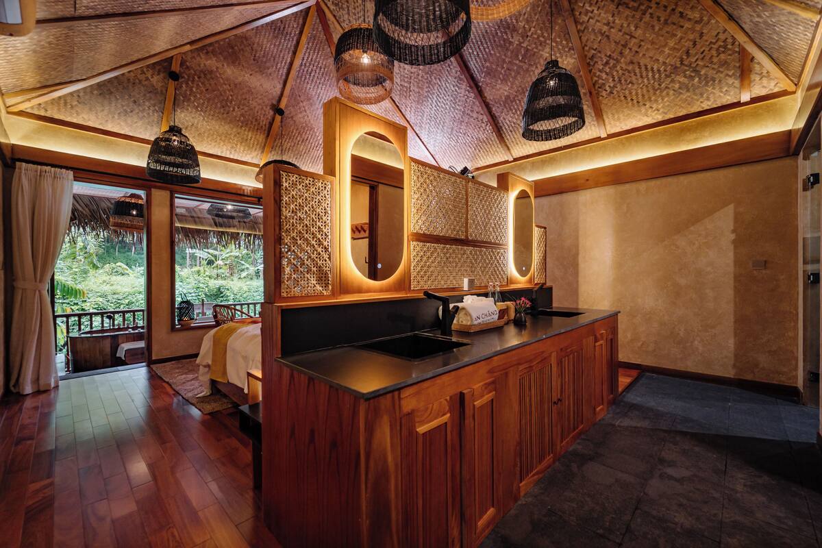 Una cocina moderna con armarios de madera, encimera negra y vistas al jardín a través de grandes ventanales.