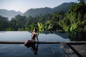 A woman sitting by a reflective infinity pool with lush greenery and mountains in the background. - An Châng Retreat & Spa (Ha Giang 1)