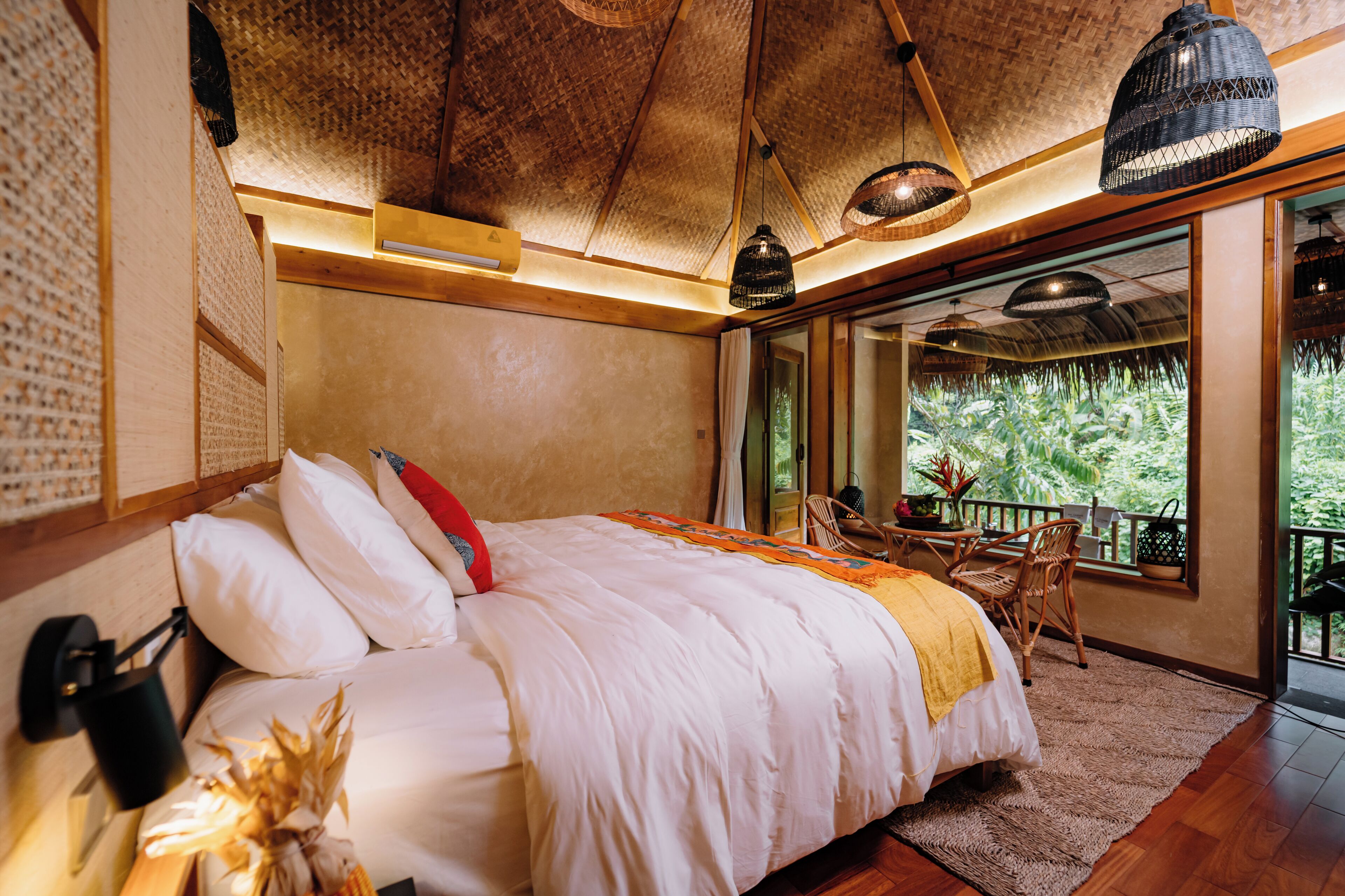 A bedroom with a large bed, a wooden ceiling, and a balcony with a view of greenery.