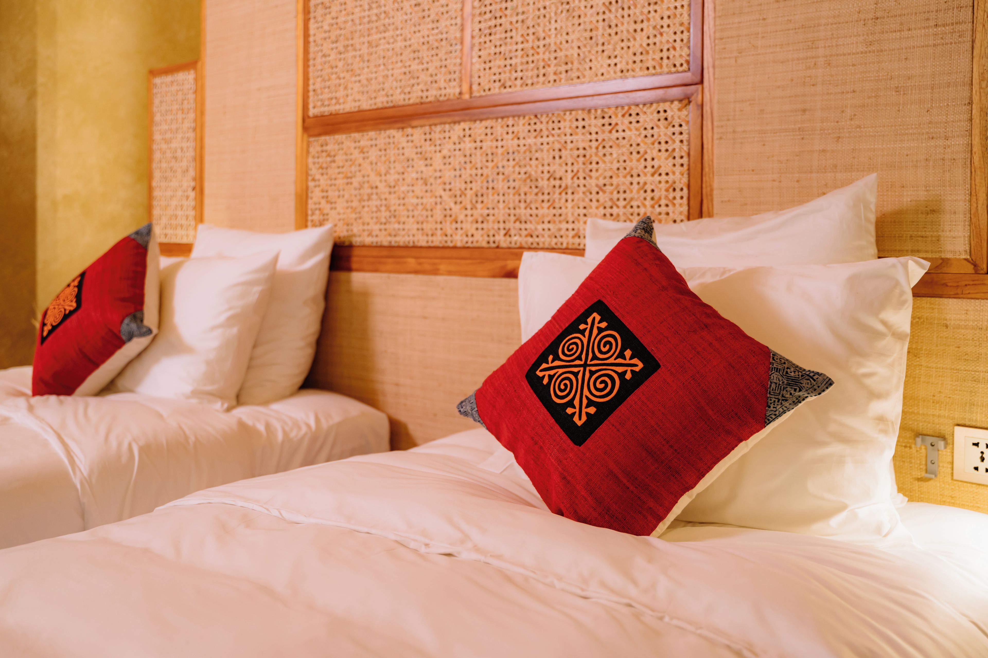 Een hotelkamer met twee bedden, elk voorzien van witte beddengoed en rode sierkussens.