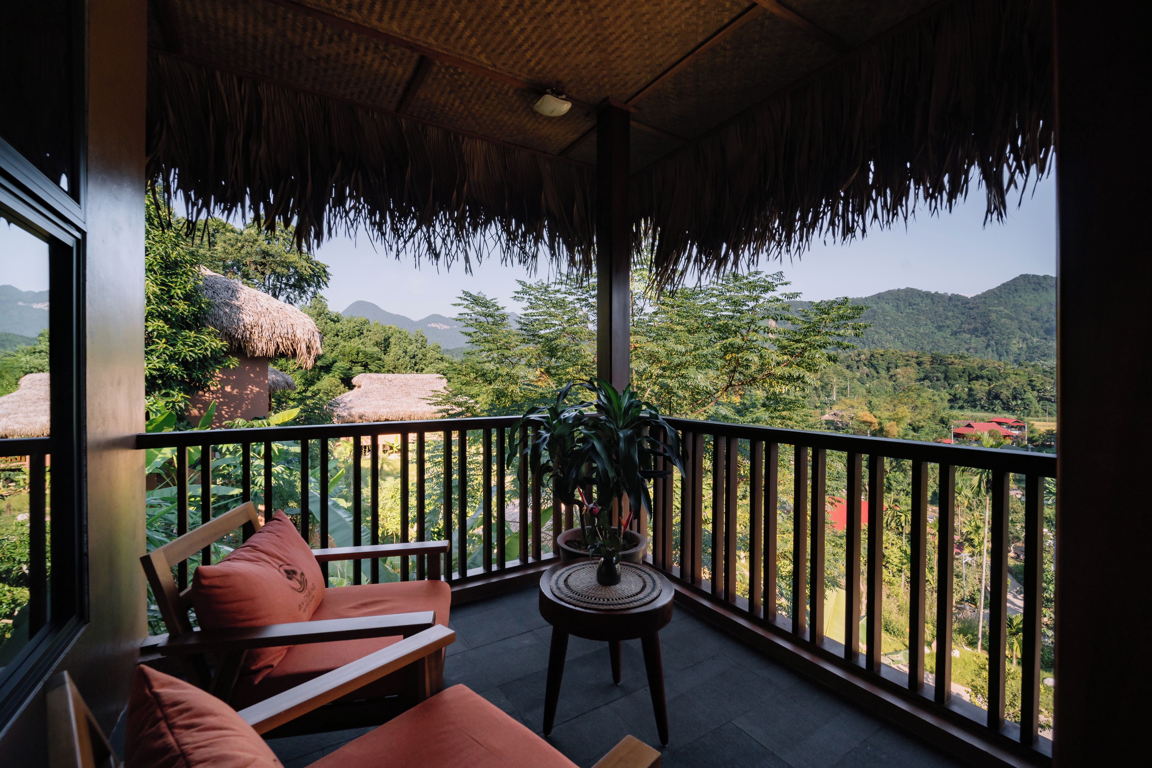 Ein Balkon mit Blick auf eine gebirgige Landschaft, ein Strohdach und eine Sitzgelegenheit mit Kissen.
