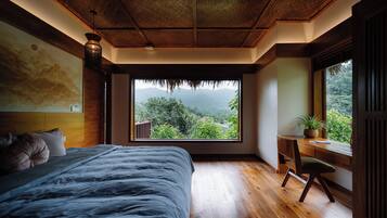 Un dormitorio con un ventanal grande, suelo de madera, una cama, un escritorio y una silla.