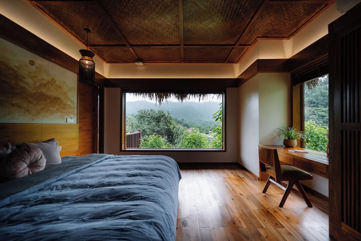 Un dormitorio con un ventanal grande, suelo de madera, una cama, un escritorio y una silla.