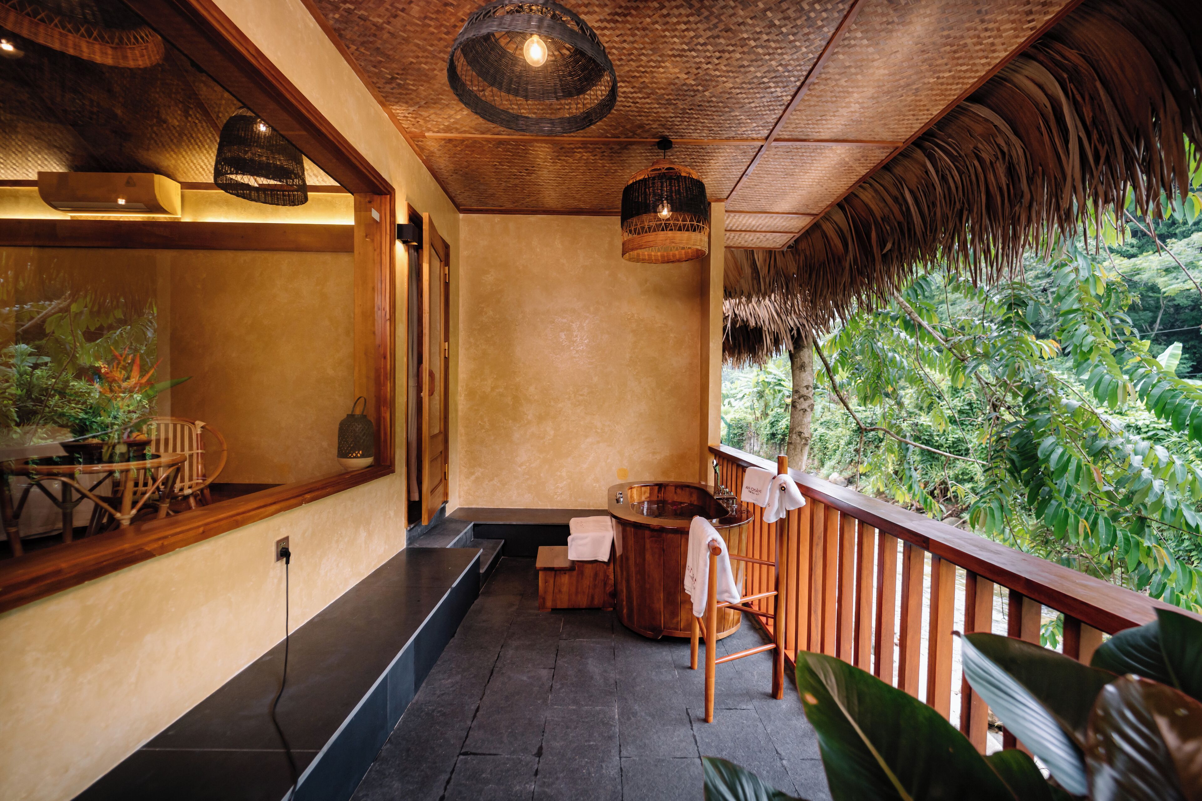A spa area with a wooden bench, a wooden bathtub, and a view of lush greenery.