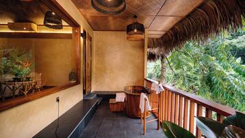 A spa area with a wooden bench, a wooden bathtub, and a view of lush greenery.