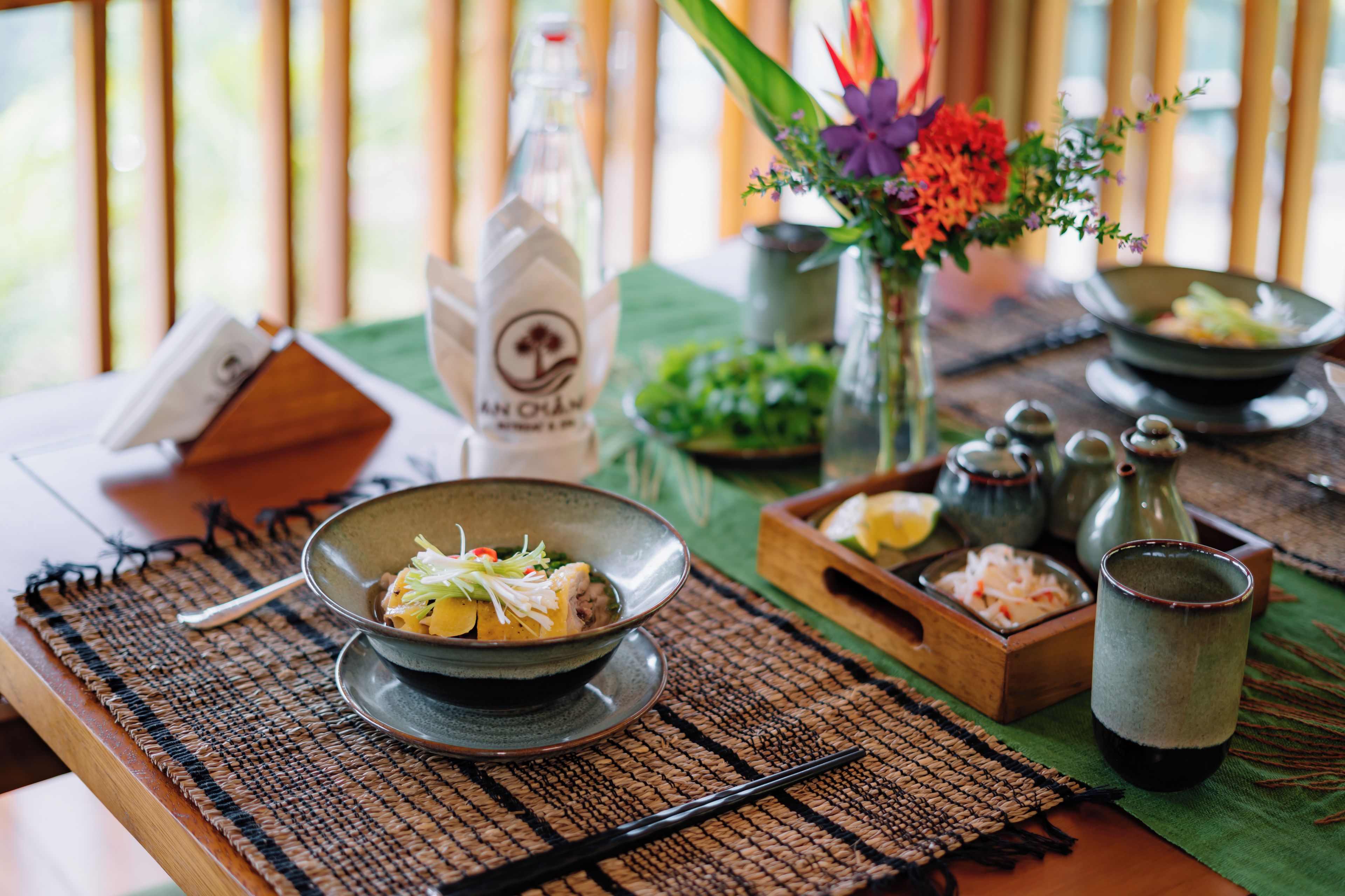 A dining table with a bowl of food, a bottle, and a vase with flowers.
