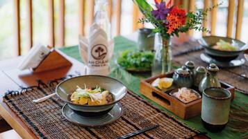 A dining table with a bowl of food, a bottle, and a vase with flowers.