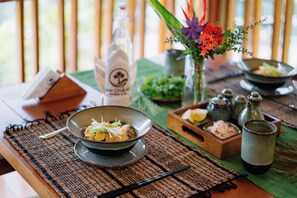 A dining table with a bowl of food, a bottle, and a vase with flowers. - An Chang Retreat & Spa (Ha Giang 1)