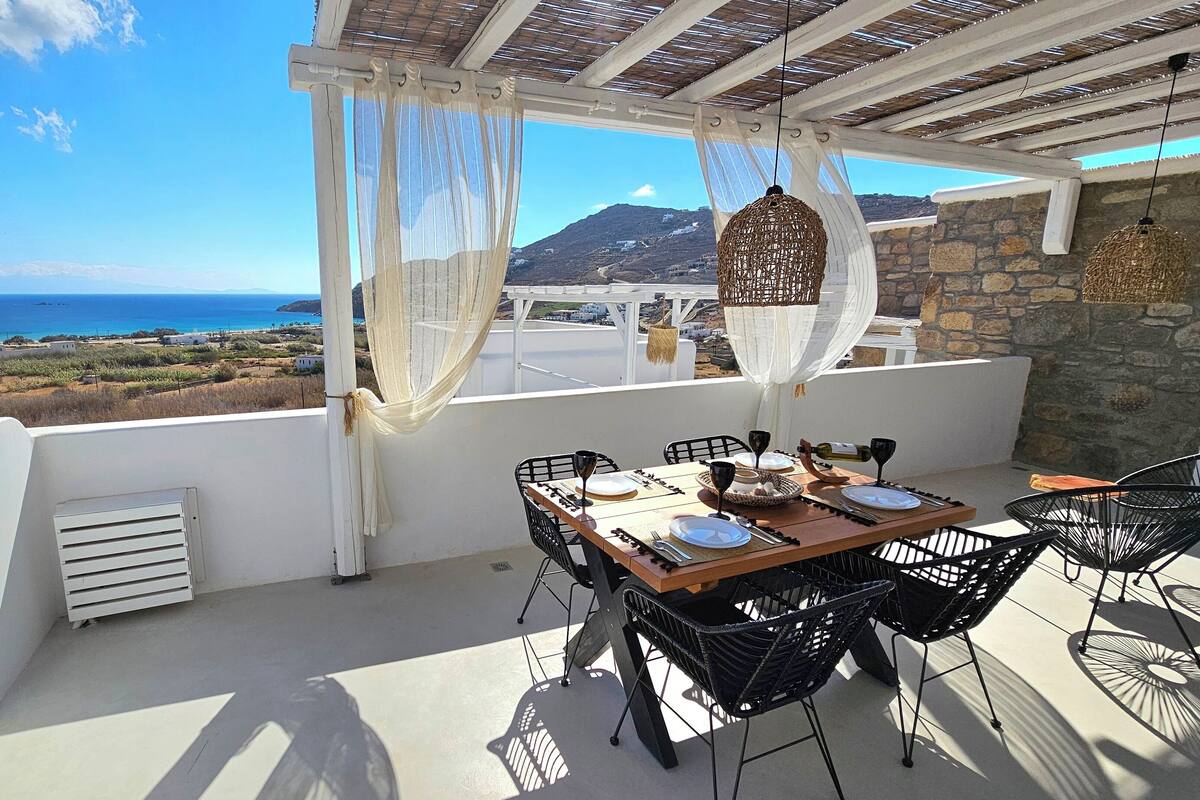 A terrace with a table set for two, overlooking a coastal landscape.