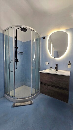 A modern bathroom with a glass-enclosed shower, a round mirror, and a wooden vanity. - Mykonos4Islands Seaside Homes and Suites (Mykonos)