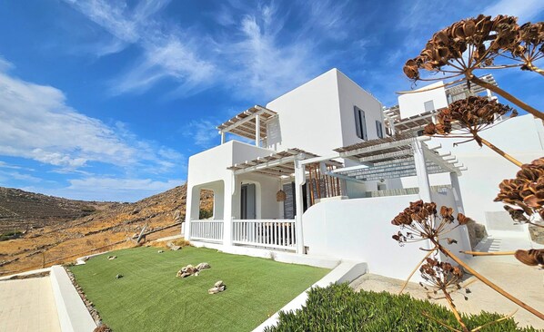 A white building with a flat roof, a balcony, and a view of a hilly landscape. - Mykonos4Islands Seaside Homes and Suites (Mykonos)