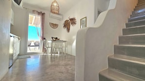 A modern interior with a staircase, a dining area with white chairs, and a view through a glass door. - Mykonos4Islands Seaside Homes and Suites (Mykonos)
