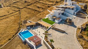A modern villa with a swimming pool, multiple levels, and a view of the surrounding hilly landscape. - Mykonos4Islands Seaside Homes and Suites (Mykonos)