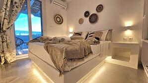 A modern bedroom with a large bed, a view of the sea, and decorative wall art. - Mykonos4Islands Seaside Homes and Suites (Mykonos)