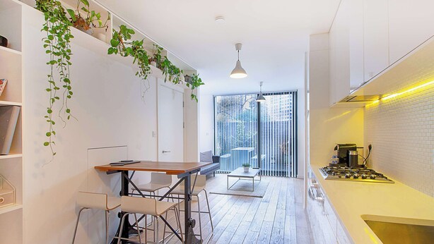 Eine moderne Küche mit Holztisch und Barhocker, einem Gasherd und einem großen Fenster mit Blick auf die Stadt.