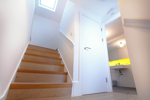 Un escalier menant à une salle de bain avec un lavabo blanc et une petite poubelle.