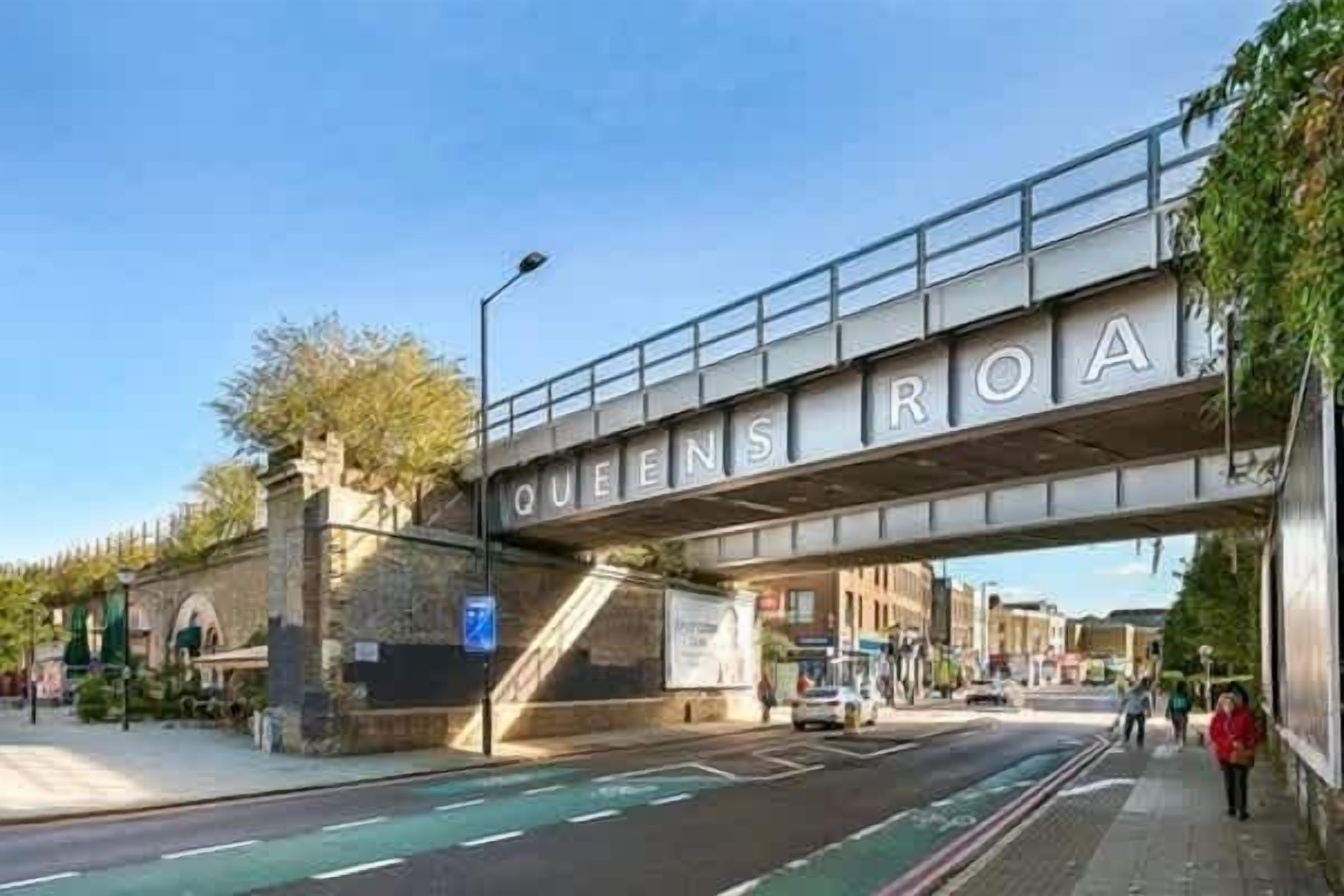 A street under a bridge with the sign 'QUEENS ROAD'.