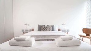 Ein modernes Hotelzimmer mit einem ordentlich bezogenen Bett, zwei Nachttischen mit Lampen und einem Holzstuhl.