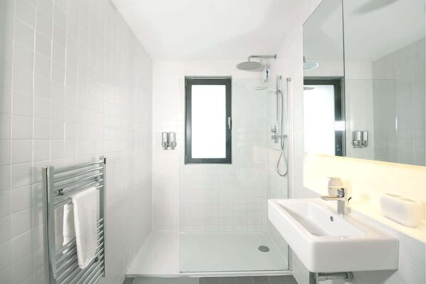 A modern bathroom with a glass shower enclosure, a white sink, and a towel rack.