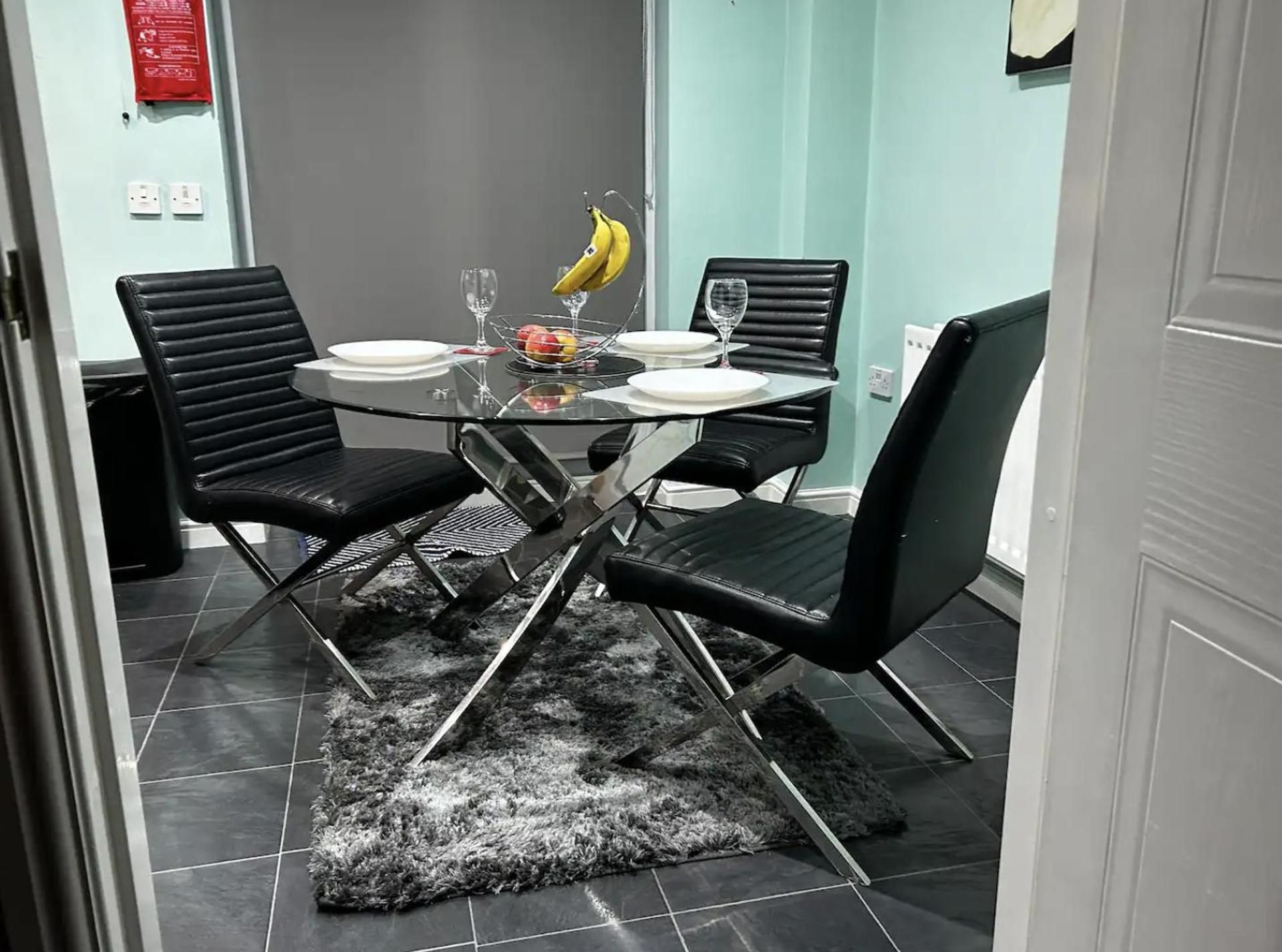 A dining area with a round glass table, black chairs, a black furry rug, and a fruit bowl with bananas.
