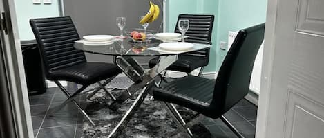 A dining area with a round glass table, black chairs, a black furry rug, and a fruit bowl with bananas.