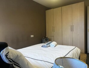 Een hotelkamer met een bed, een kledingkast en een klein tafeltje met een tas en een opgerolde handdoek.