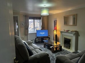 Una sala de estar con un conjunto de sofás, un televisor, una chimenea y una ventana con cortinas.