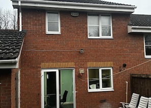 Een herenhuis met twee verdiepingen, een garagepoort, een kleine aangebouwd garage, en een zichtbare schotelantenne.