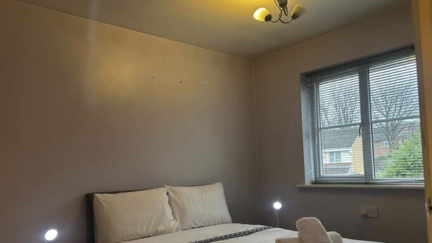 Ein Schlafzimmer mit einem Bett, Nachttischlampen und einem Fenster mit Jalousien.