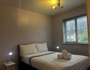 Een slaapkamer met een bed, bedlampen en een raam met jaloezieën.