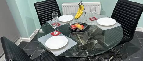 Un coin repas avec une table en verre, des chaises noires et un saladier rempli de fruits.