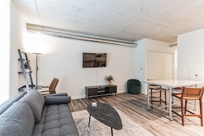 Ein modernes Wohnzimmer mit einer Couch, einem Couchtisch, einem Fernseher, einer Essecke mit Tisch und Stühlen und einem Schrank.