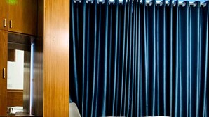 A hotel room with a wooden bed frame, a large window with dark curtains, and a wooden wardrobe. - Hotel City View (Dhaka)