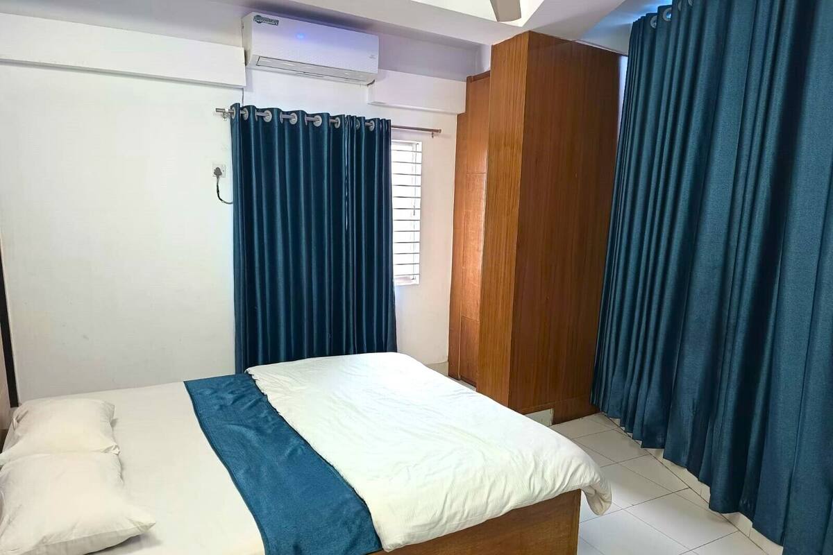 A bedroom with a bed, a wooden wardrobe, and a window with curtains.