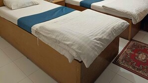 A hotel room with two single beds, a wooden headboard, a ceiling fan, a wall-mounted light fixture, and a red patterned rug on the floor. - Hotel City View (Dhaka)