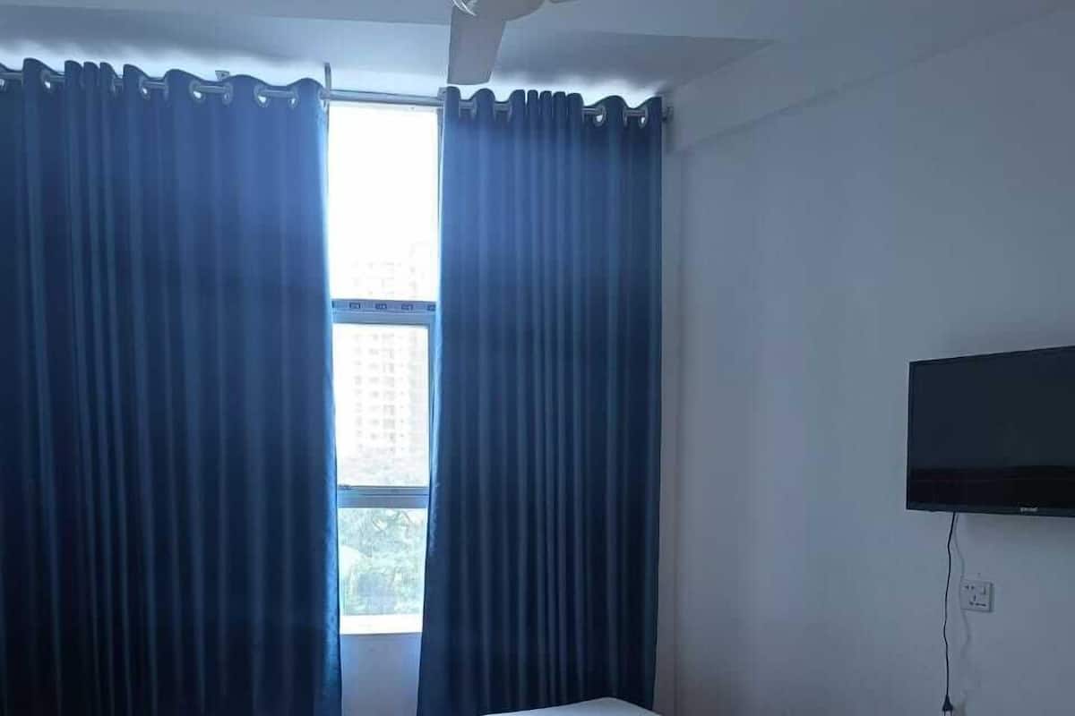 A bedroom with a bed, curtains, a ceiling fan, a TV, and a window.