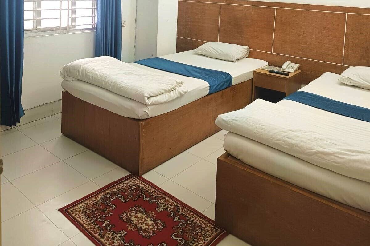 A hotel room with two beds, a wooden headboard, a red patterned rug, a ceiling fan, and a window with blue curtains.