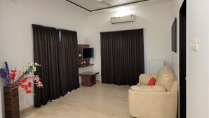 Un soggiorno con un divano color beige, una televisione a schermo piatto, una ventola a soffitto e un condizionatore d'aria.
