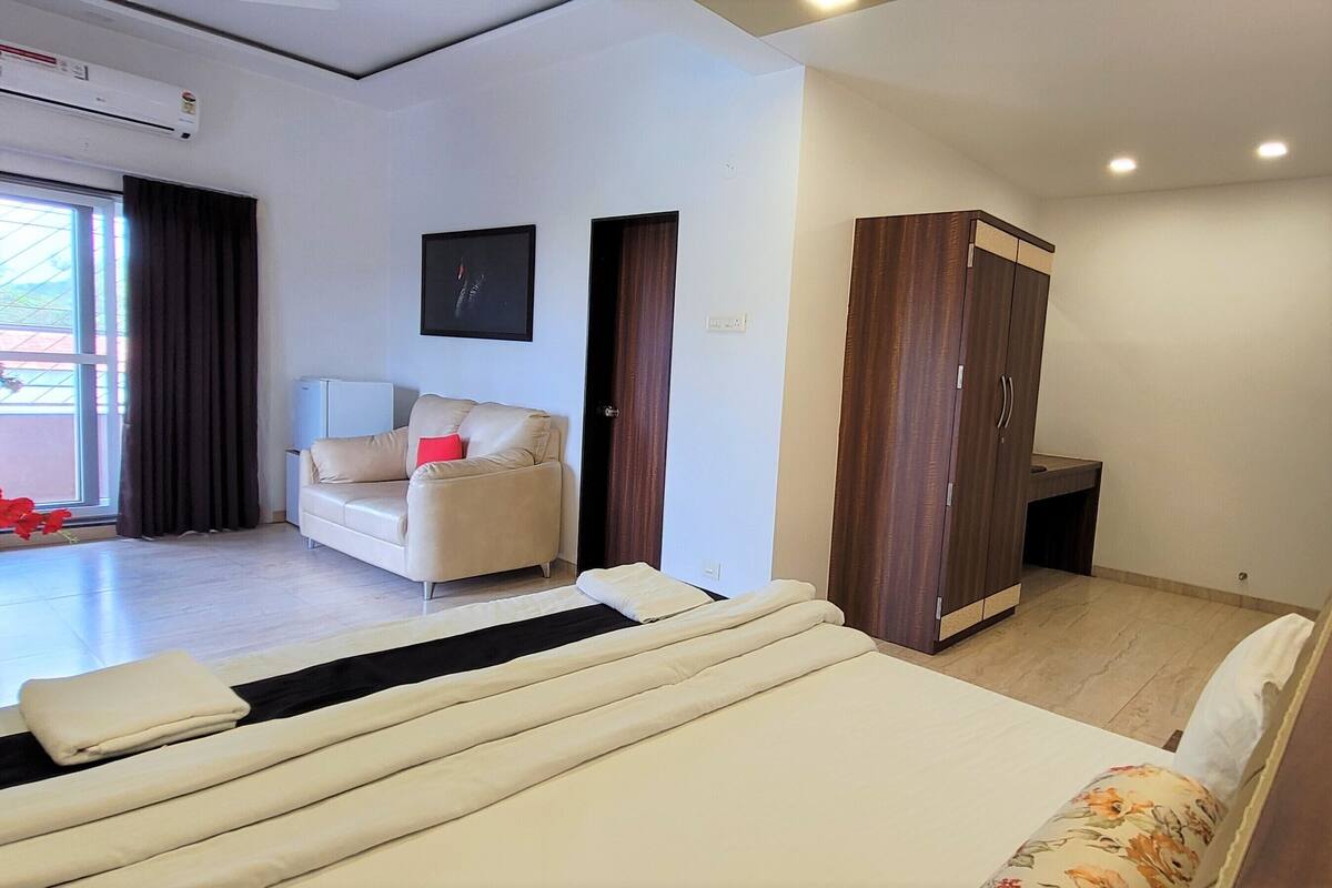 A modern bedroom with a large bed, a sofa, a wardrobe, and a window with curtains.