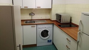 Uma cozinha compacta com armários brancos, máquina de lavar, micro-ondas e frigorífico.