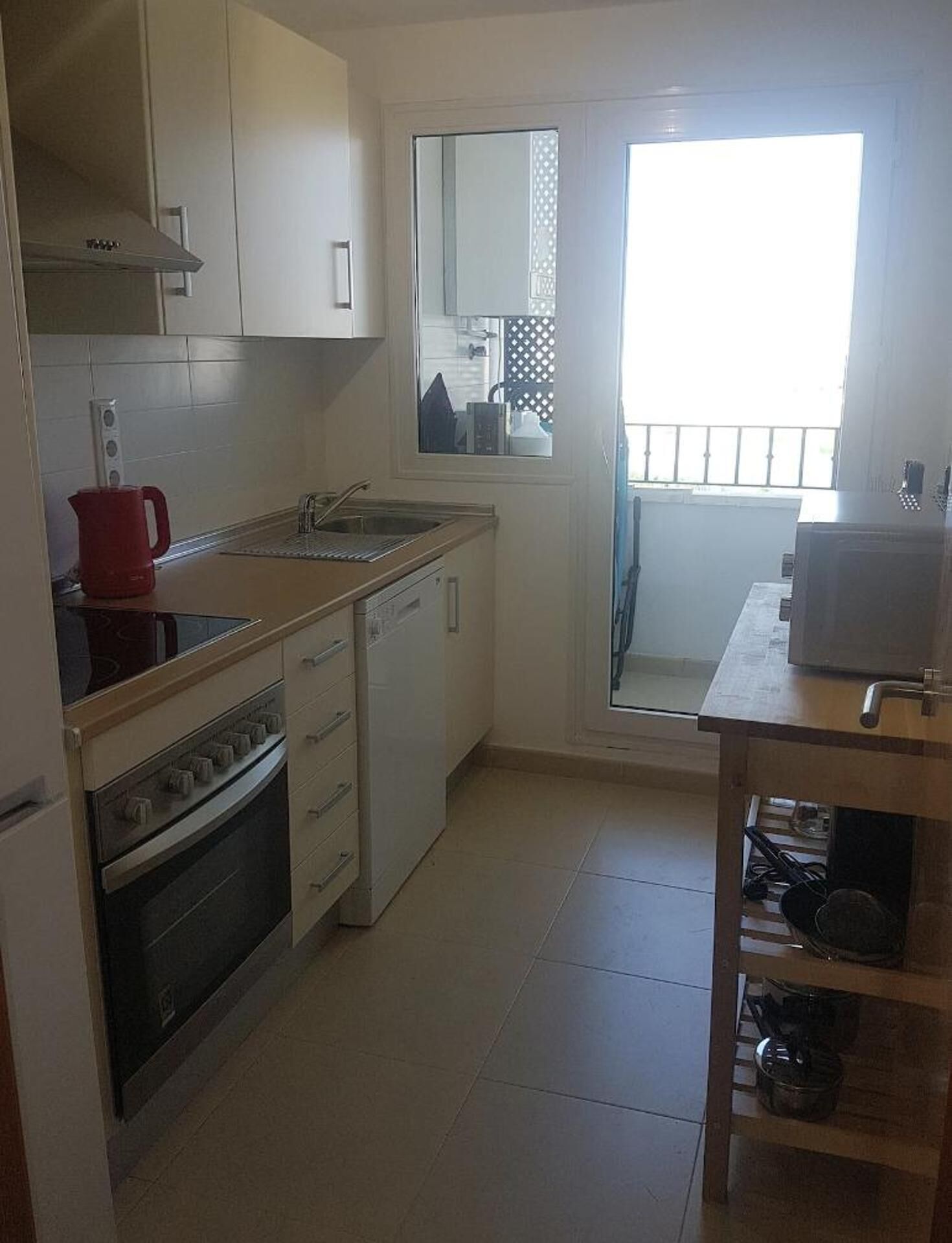 A compact kitchen with a stove, oven, sink, and a small window.