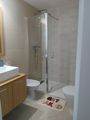 A modern bathroom with a glass-enclosed shower, a white sink, and a toilet.