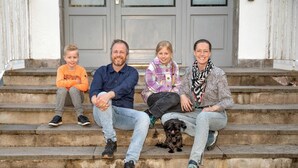 Eine vierköpfige Familie sitzt auf Steinstufen vor einem Gebäude mit einer grauen Tür.