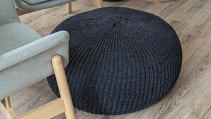 Ein Wohnzimmer mit grauem Sofa, Hocker in Schwarz, Kamin in Schwarz und Holzboden.