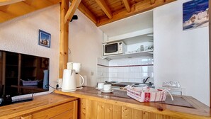 A kitchen with wooden cabinets, a microwave, and a coffee maker. - Cozy apartment near slopes with parking (Les Menuires)