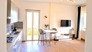 Una cucina moderna con zona pranzo, TV a parete e una porta scorrevole in vetro che dà su un balcone.