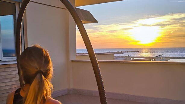 Una persona su una sedia a dondolo con vista su un tramonto dal balcone.