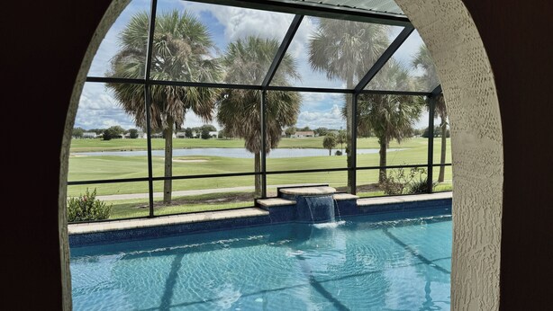 A pool with a view of a golf course and palm trees.